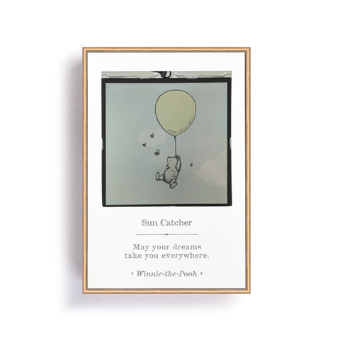 Glass suncatcher with an image of Winnie-the-Pooh hanging from a yellow balloon with bees flying around him. The catcher is mode of square glass with a black metal frame. This image is of the of the product in it's box.