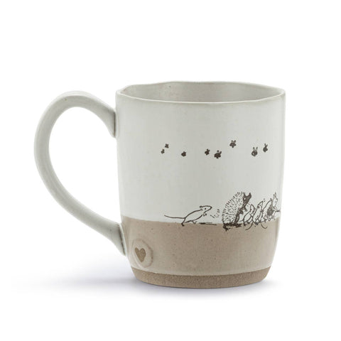 A handmade ceramic mug with a two-tone design, featuring a white upper half decorated with small black illustrations of stars, bees, a mouse, and hedgehogs, and a textured beige lower half with a small heart detail near the base.