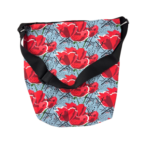 n everyday bag adorned with a vibrant red poppy flower pattern on a blueish gray background and featuring a black strap. 