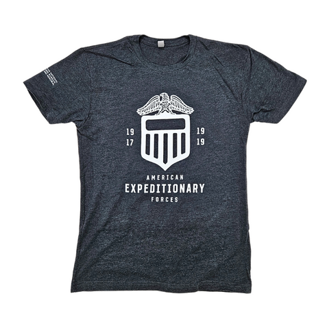 A charcoal gray tshirt with a white insignia for the American Expeditionary Forces placed in large font in the center. This looks like a shield with four vertical lines and an eagle with spread wings sitting on top. On the right sleeve of the shirt is the logo for the National WWI Museum and Memorial.