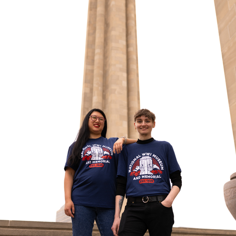 Two people wearing a dark blue t-shirt that depicts the Liberty Memorial Tower with poppy flowers. Arching over the tower is the text 'National WWI Museum and Memorial'. The Liberty Memorial Tower is in the background.