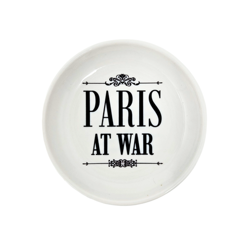 A round white trinket dish with the logo for the Paris at War Exhibition. The text is in black.