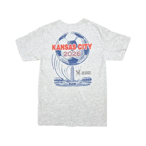 The back side of a light gray tshirt with the text Kansas City 2026 in retro font with an illustration of the Liberty Memorial Tower and a soccer ball in the background. The design is in red and blue,