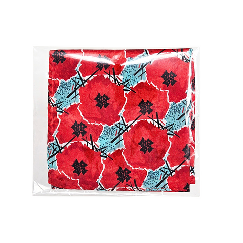 This image depicts a silk pocket square with digitally manipulated poppies that are repeated and stacked on one another with the National WWI Museum and Memorial Intersections logo interlaced between. The pocket square has a color theme of red poppies, with light blue accents. It folded into quarters and placed inside of clear plastic packaging that it comes in, and placed on a white back drop.