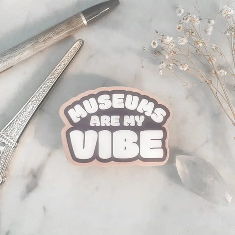 A sticker with the text MUSEUMS ARE MY VIBE sits next to a pen, dried flowers, and a crystal on a light background—a perfect scene for any museum lover who cherishes art and culture.