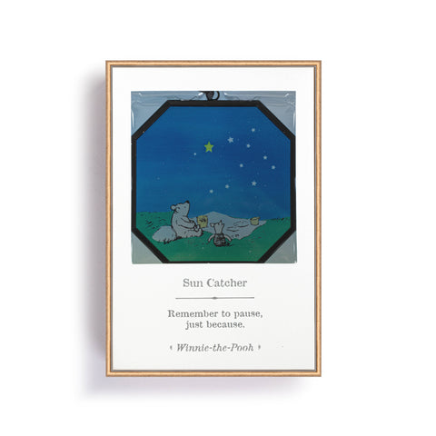 Glass suncatcher with an image of Winnie-the-Pooh and piglet having a picnic at night while looking at the stars. The catcher is mode of octagonal glass with a black metal frame. This image is of the product in the box.