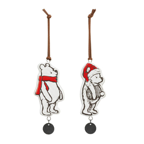 Two Winnie-the-Pooh Christmas ornaments. They are made of ceramic and have a small round metal disk hanging from them with a heart engraved on it. One ornament has Pooh Bear wearing a red scarf and the other a red hat. This picture shows them from the back.