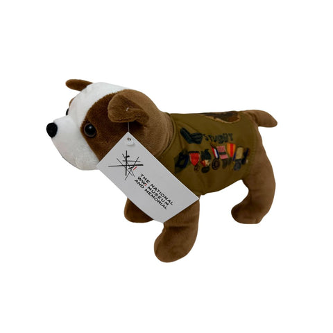 Image of a plush dog that is made in the likeness of Sergeant Stubby, the hero war dog from WWI. The dog is dark brown with a patch of white that runs from the top of its head down to its muzzle, and is wearing a tan colored vest that is adorned with badges and medals along the side. The side also reads Stubby just above the badges and medals. In this image, the dog is facing to the left with a tag that depicts the logo for the National WWI Museum and Memorial hanging from its ear. 